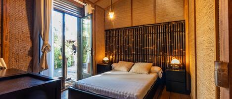 Un dormitorio con cama, mesitas de noche, una ventana y vistas al verde exterior.