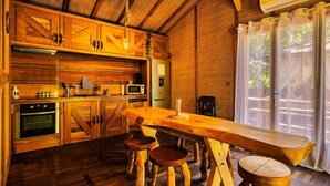 A rustic kitchen with wooden cabinets, a dining table, stools, and a view of the outdoors through a window. - Chalet "Bangli" with Private Terrace and Wi-Fi (LACANAU)
