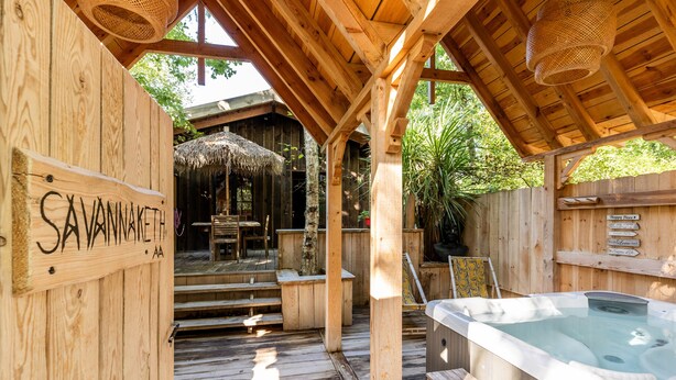 Eine Holzterrasse mit Whirlpool, Holzbanken und einem Schild mit der Aufschrift 'SAVANNAKETH'.
