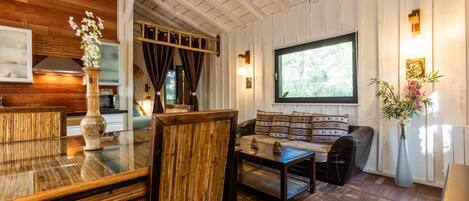 A wooden-paneled room with a glass dining table, a sofa with patterned cushions, and a large window.