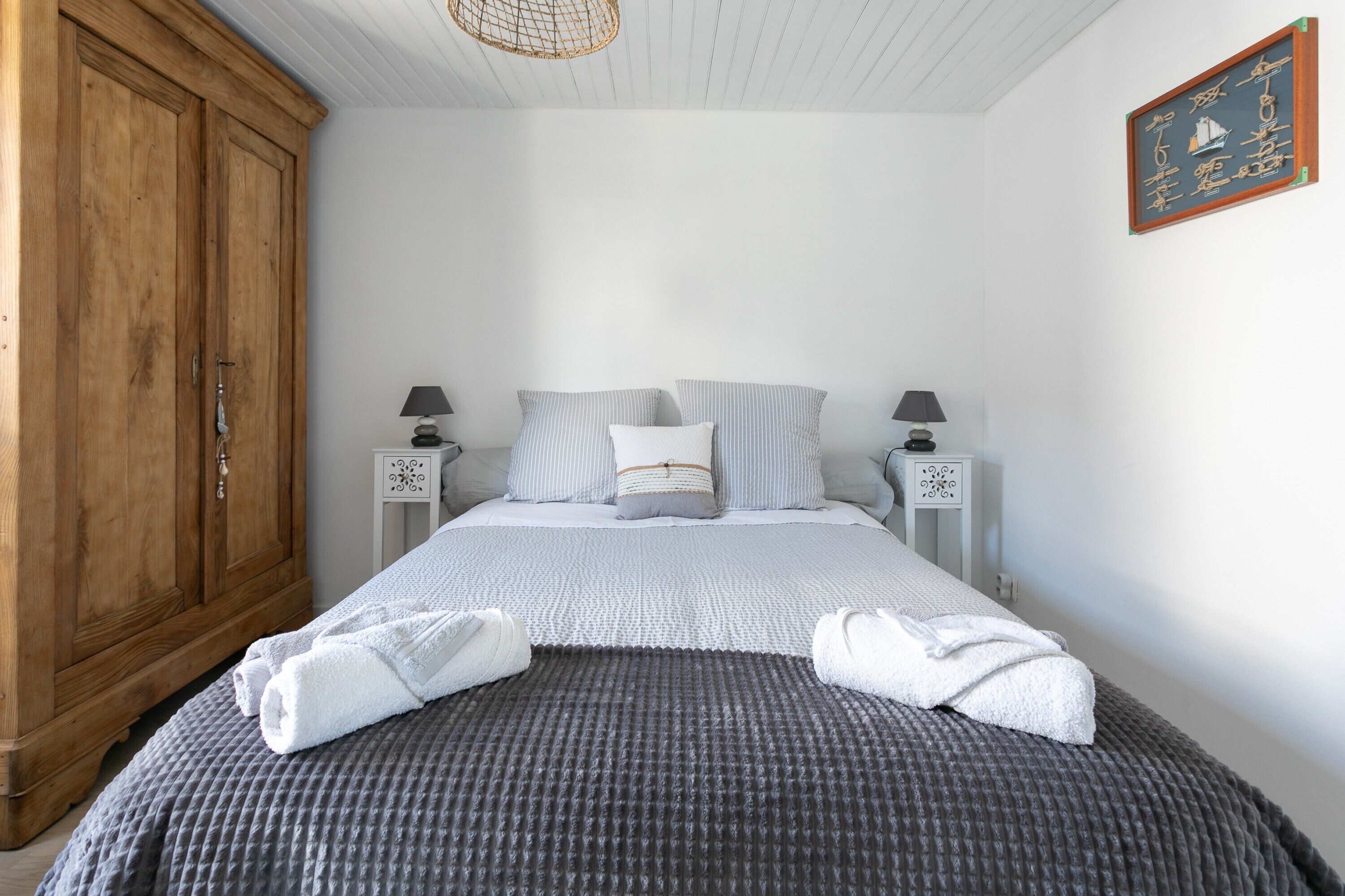 Une chambre avec une grande armoire en bois, un lit avec une literie à rayures, deux tables de chevet avec des lampes et une œuvre d’art accrochée au mur.