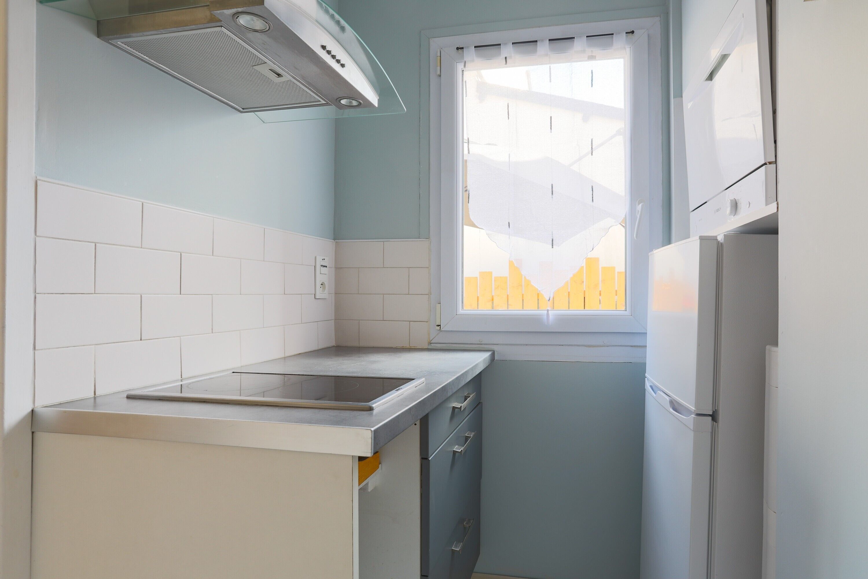 Une cuisine compacte avec une fenêtre, des placards blancs, une cuisinière encastrée et un réfrigérateur.