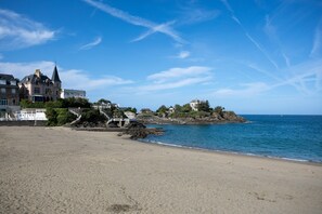 Une plage avec un grand bâtiment, un promontoire rocheux et l’océan.