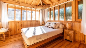 A wooden room with a bed, a nightstand, and large windows.
