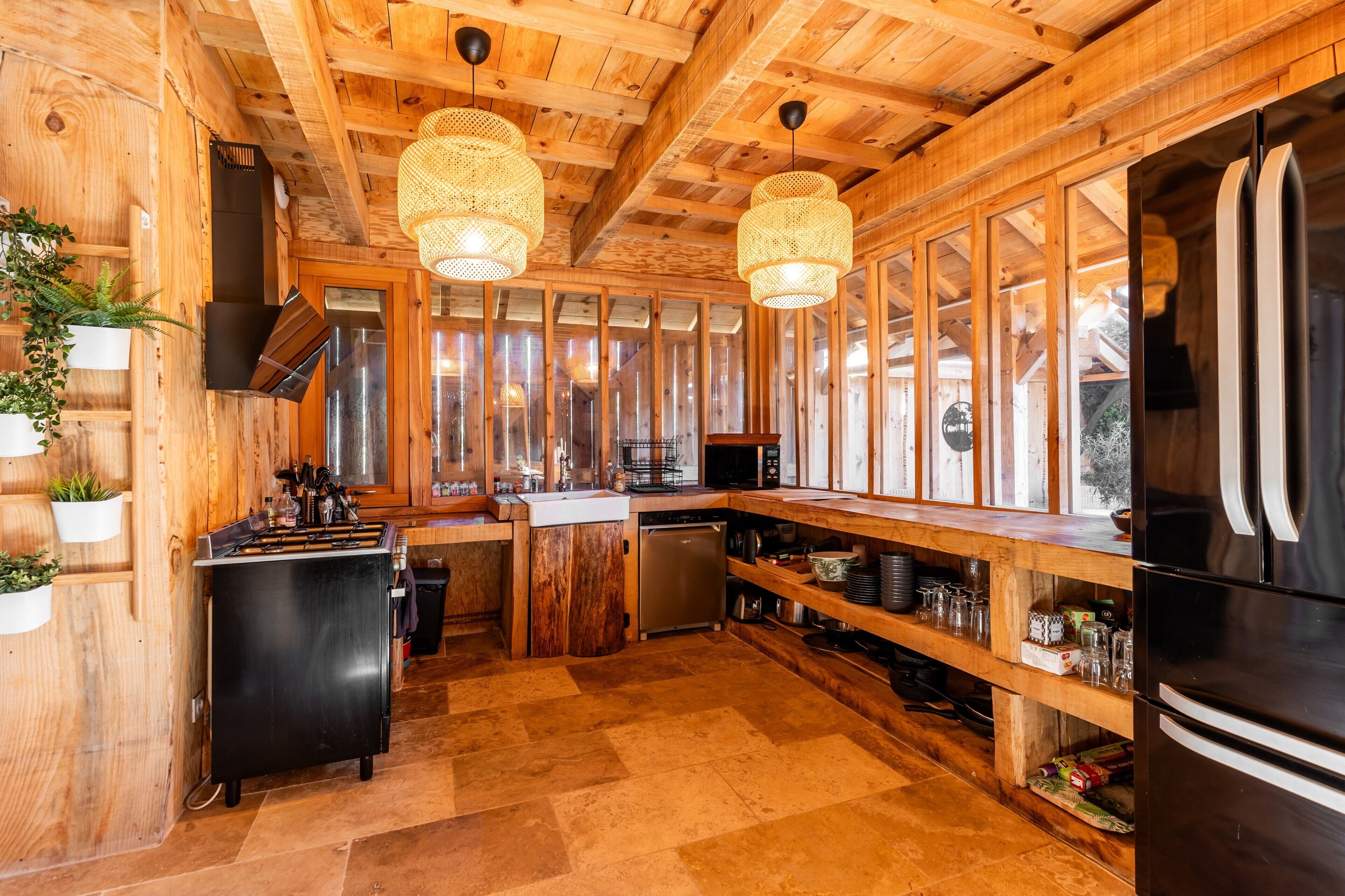 A wooden interior with a kitchen area, including a stove, refrigerator, and hanging lights.