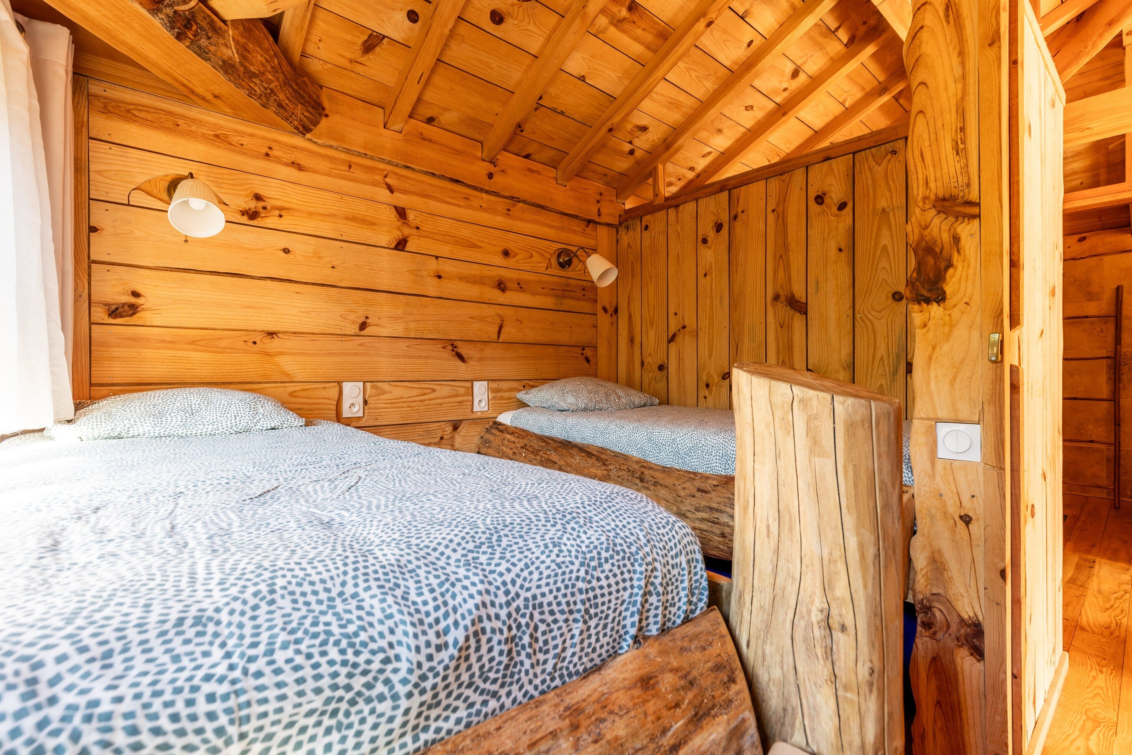 Puuinen mökki, jossa on kaksi sänkyä, ja jokaisessa sängyssä on kuviollinen vuodevaatesetti.