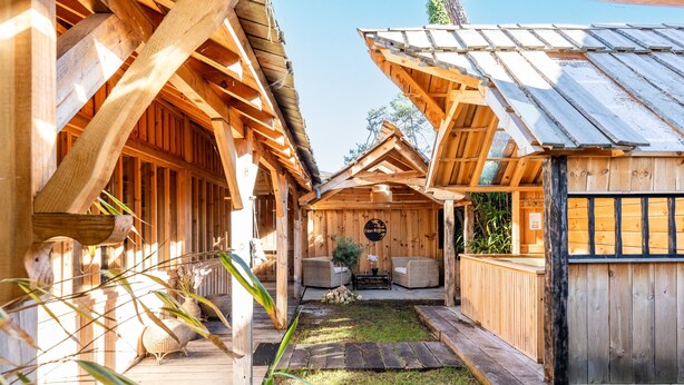 A wooden cabin with a porch, a central seating area, and a small garden.