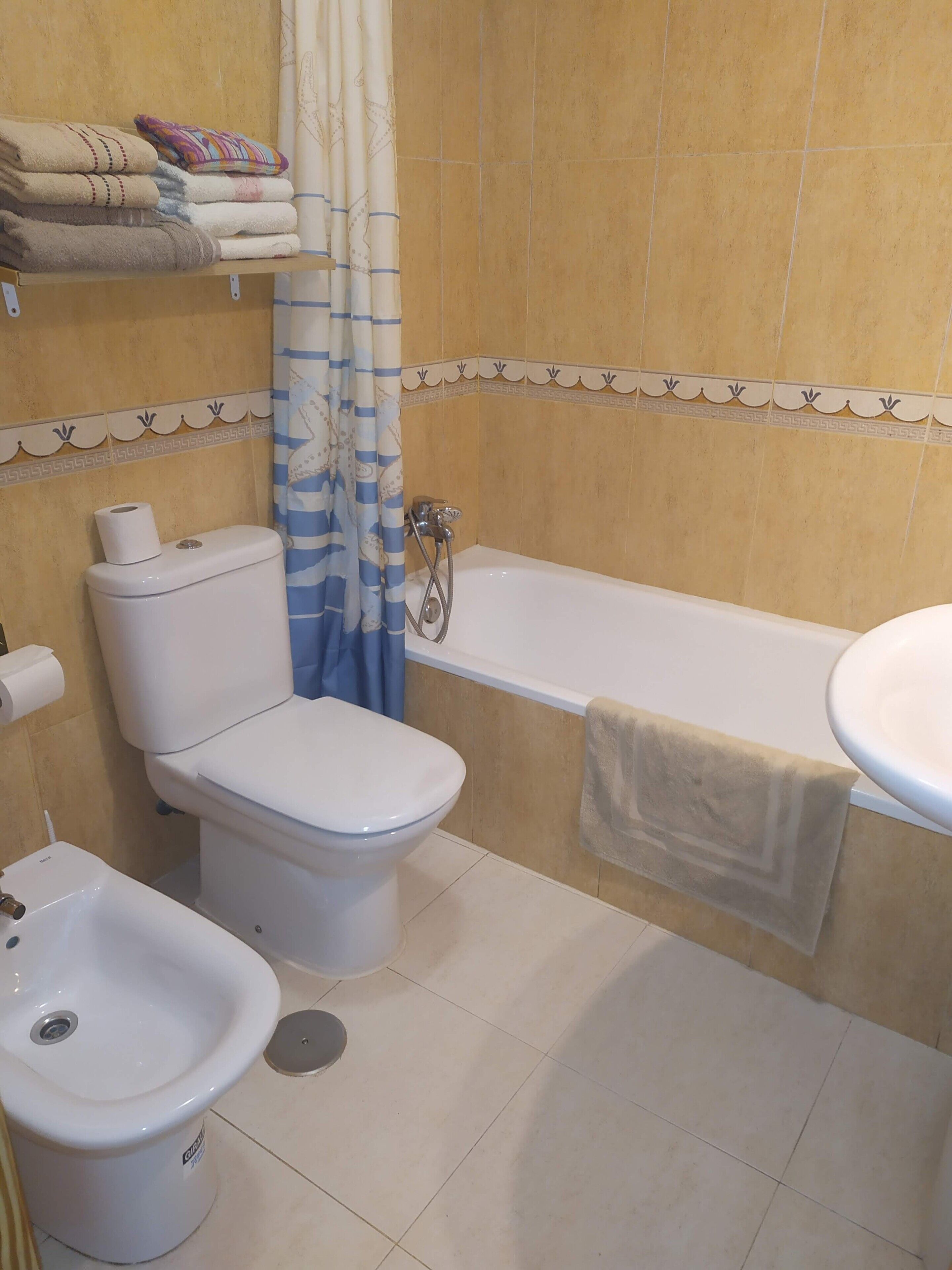 Un baño con inodoro, bidé, bañera y un perchero con toallas.
