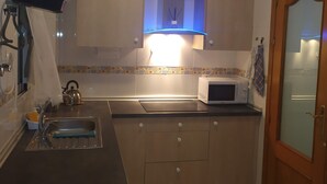 A compact kitchen with a sink, kettle, microwave, and a cabinet with a blue light.