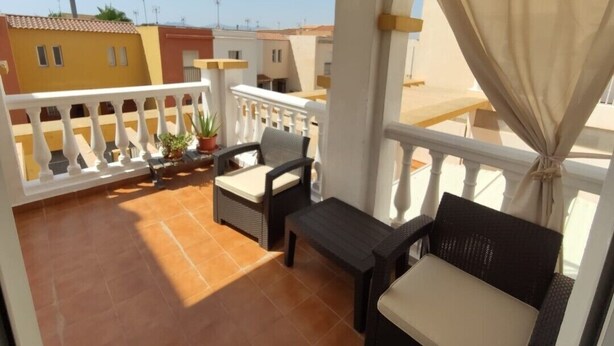 A balcony with a white railing, a table, two chairs, and a potted plant.