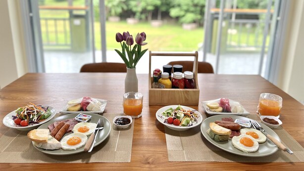 A breakfast table with various dishes, a vase with flowers, and condiments.