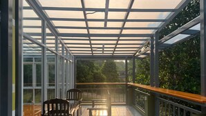 A covered outdoor area with a glass enclosure, wooden chairs, and a tiled floor.
