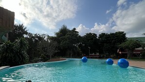 A swimming pool with clear water, surrounded by trees and a building in the background.