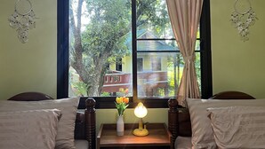 A room with two beds, a bedside table with a lamp, a window with curtains, and an air conditioner on the wall.