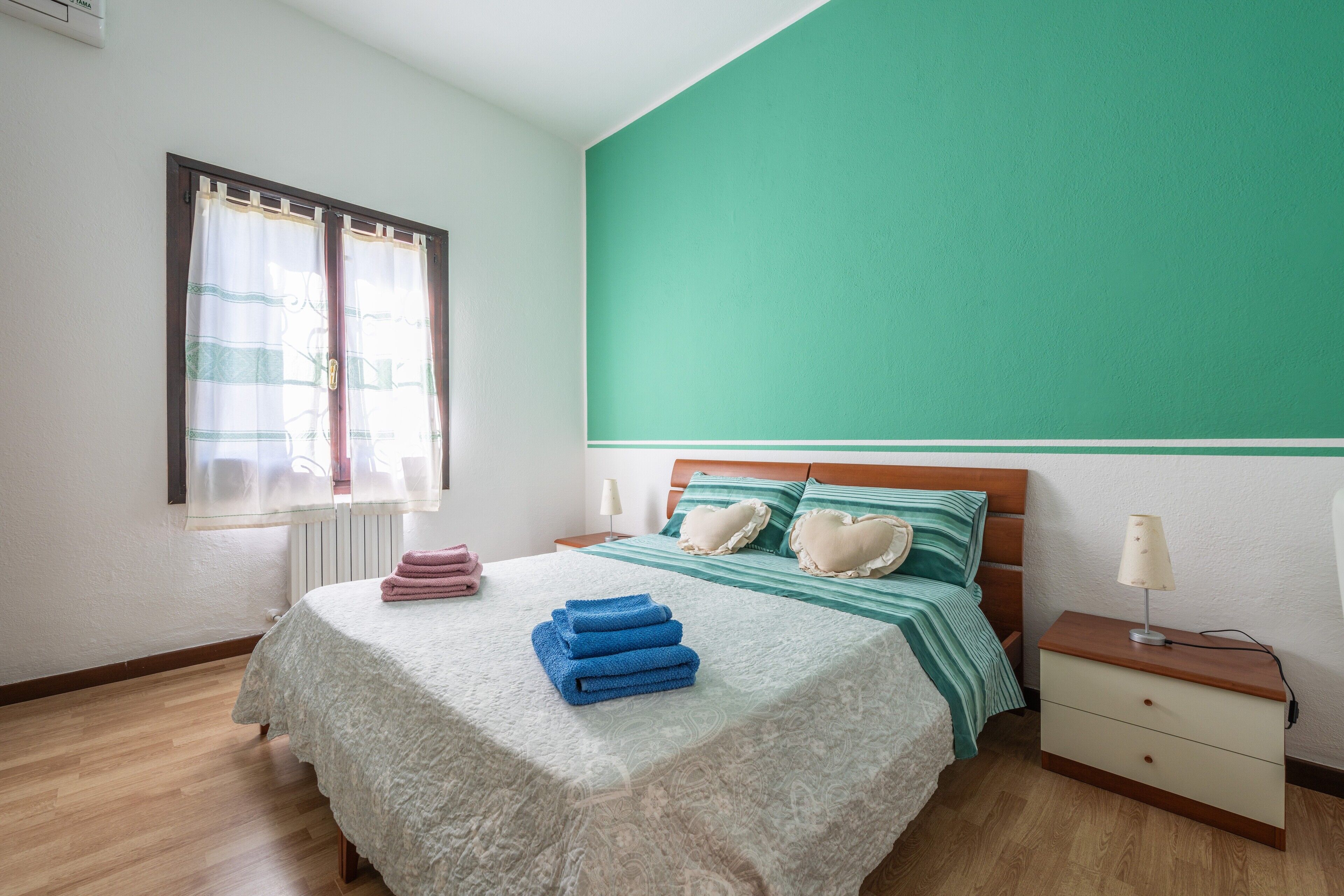 A bedroom with a bed, a nightstand, a lamp, and a window with curtains.