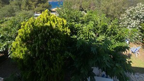 A garden with a stone table and chairs, surrounded by lush greenery and a view of a body of water and hills in the distance. - Petite Villa Attrayante vue mer Avec Jardin et Parking Privé (Saint-Raphaël)