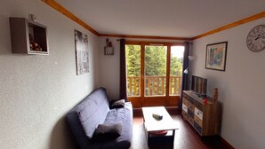 Ein Wohnzimmer mit einer Couch, einem Couchtisch, einer TV-Konsole und einem Balkon mit Holzgeländer.
