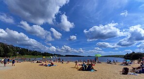 Une plage où des gens se prélassent au soleil et se baignent, un ciel dégagé et un lac en arrière-plan.