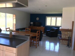 A kitchen with a wooden table and chairs, a dining area with a blue wall and a fireplace, and a living room with a sofa and television.