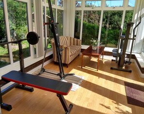 Exercise and unwind in a room with a view of lush greenery, featuring a weightlifting area and a comfortable seating area.