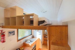 Habitación compacta con literas, un kitchenette pequeño, una ventana y un extintor.