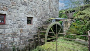 A stone building with a large water wheel, a metal fence, and a grassy area. - Tiny House 'Très Jolie Tout Confort' with Private Terrace, Private Garden and Wi-Fi (Prat)