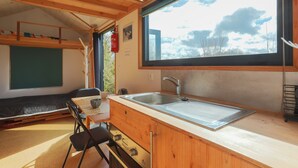 A wooden cabin interior with a kitchen area, a dining table, and a bunk bed. - Tiny House 'Très Jolie Tout Confort' with Private Terrace, Private Garden and Wi-Fi (Prat)