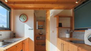 A compact kitchen with wooden cabinets, a sink, a clock, and a washing machine. - Tiny House 'Très Jolie Tout Confort' with Private Terrace, Private Garden and Wi-Fi (Prat)