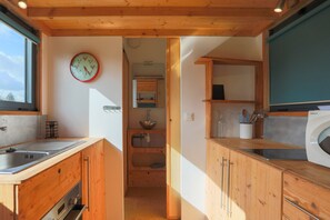 Une cuisine de taille réduite, avec des meubles de rangement en bois, un évier, une horloge et un lave-linge.