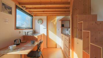 A kitchen with wooden cabinets, a dining table, chairs, a kettle, a clock, and a window.