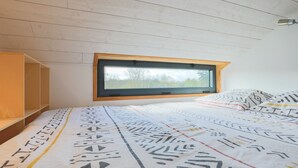 A bedroom with a bed, a window, and a wooden ceiling. - Tiny House 'Très Jolie Tout Confort' with Private Terrace, Private Garden and Wi-Fi (Prat)