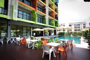 Zona de piscina exterior con varias mesas y sillas, rodeada por un edificio de varios pisos con balcones.