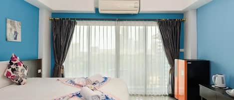 A hotel room with a bed, a desk, a kettle, and a window with curtains.