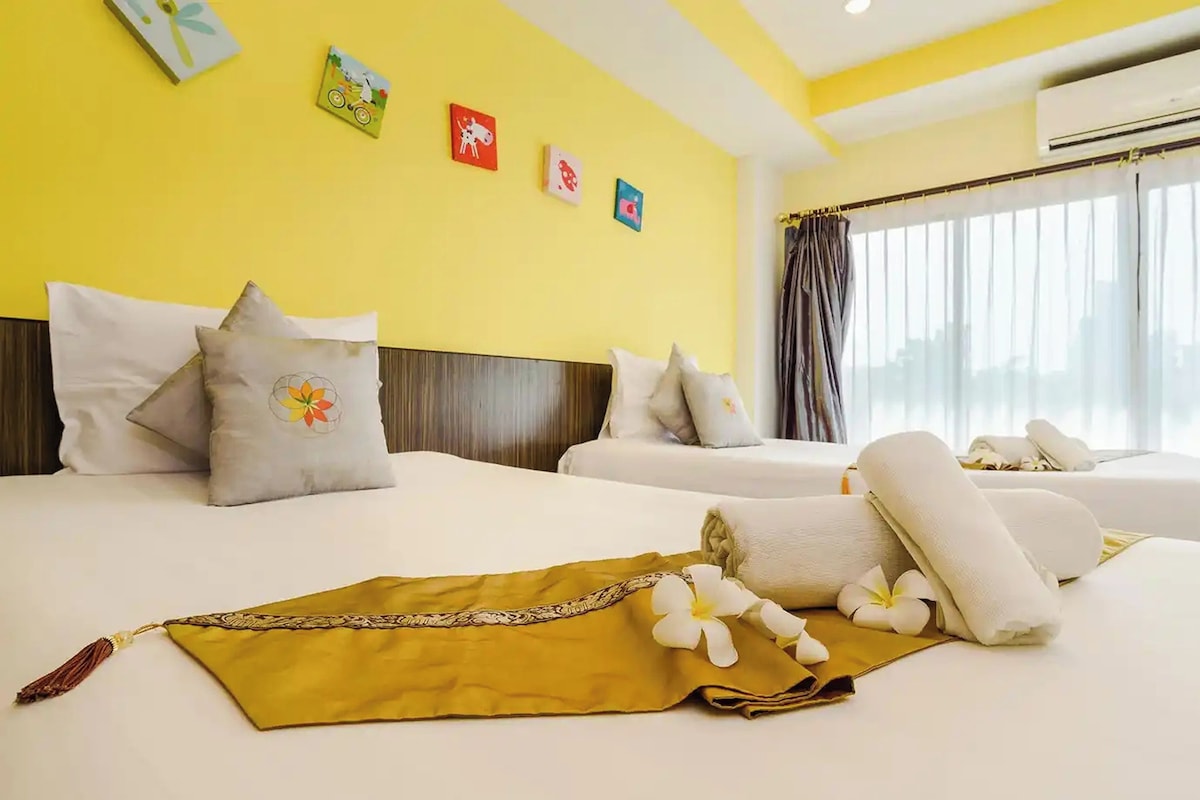Habitación de hotel con dos camas, pared amarilla y ventana con cortinas.
