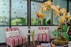 A room with two striped chairs, a small table, and a large window with a view of greenery outside. - Stay Resort Pattaya (Pattaya)