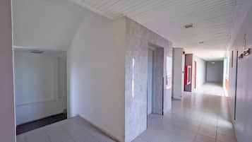 Un pasillo amplio con paredes blancas y suelo de baldosas, que conduce a varias habitaciones.