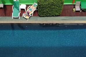 Une piscine dont le bord est recouvert de carreaux et qui est entourée d’une bordure verte.