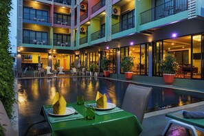 Un hotel de varios pisos con piscina, mobiliario exterior y balcones.
