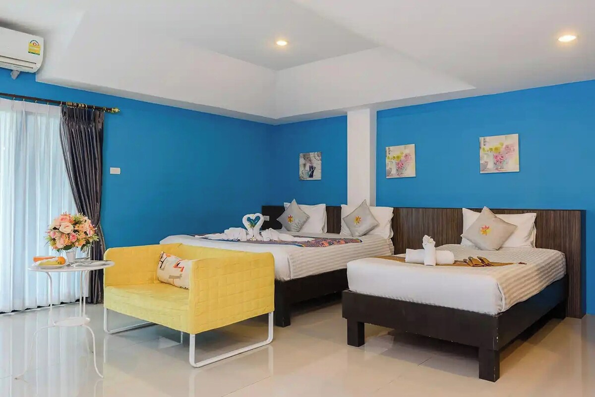 Habitación de hotel con dos camas, un sillón amarillo y una mesita con un florero.