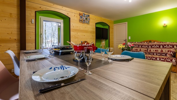 Ein Essbereich mit einem Holztisch, gedeckt für vier Personen, einem roten Topf und einer blauen Couch im Hintergrund.