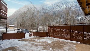 Ein verschneiter Innenhof mit Holzpforte, ein Gebäude mit schneebedecktem Dach und einem Berg im Hintergrund.
