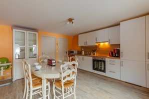 A compact kitchen with white cabinets, a microwave, a stove, and a dining area with a round table and chairs.