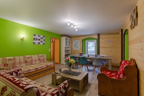 Une pièce comprenant un canapé, une table à manger avec des chaises, un coin cuisine et un mur en bois sur lequel est accroché un panneau.
