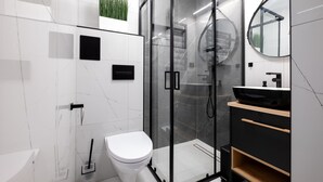 Un baño moderno con cabina de ducha de vidrio, inodoro blanco y lavabo negro sobre encimera de madera.