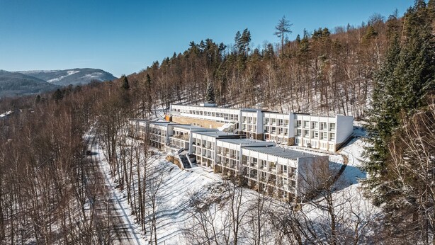 Un hotel moderno de varios pisos, rodeado por un bosque nevado y montañas.