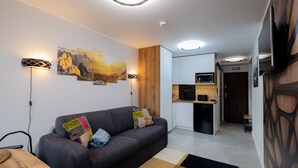 Una sala de estar moderna con un sofá gris, cojines coloridos, un muro de acento de madera y una zona de cocina con microondas y lavavajillas.