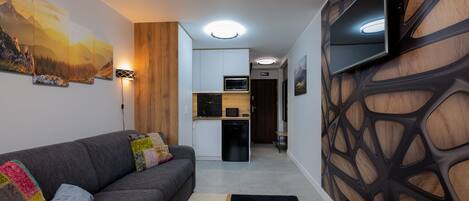 Una sala de estar moderna con un sofá gris, cojines coloridos, un panel de madera decorativo y un televisor de pantalla plana montado en la pared.