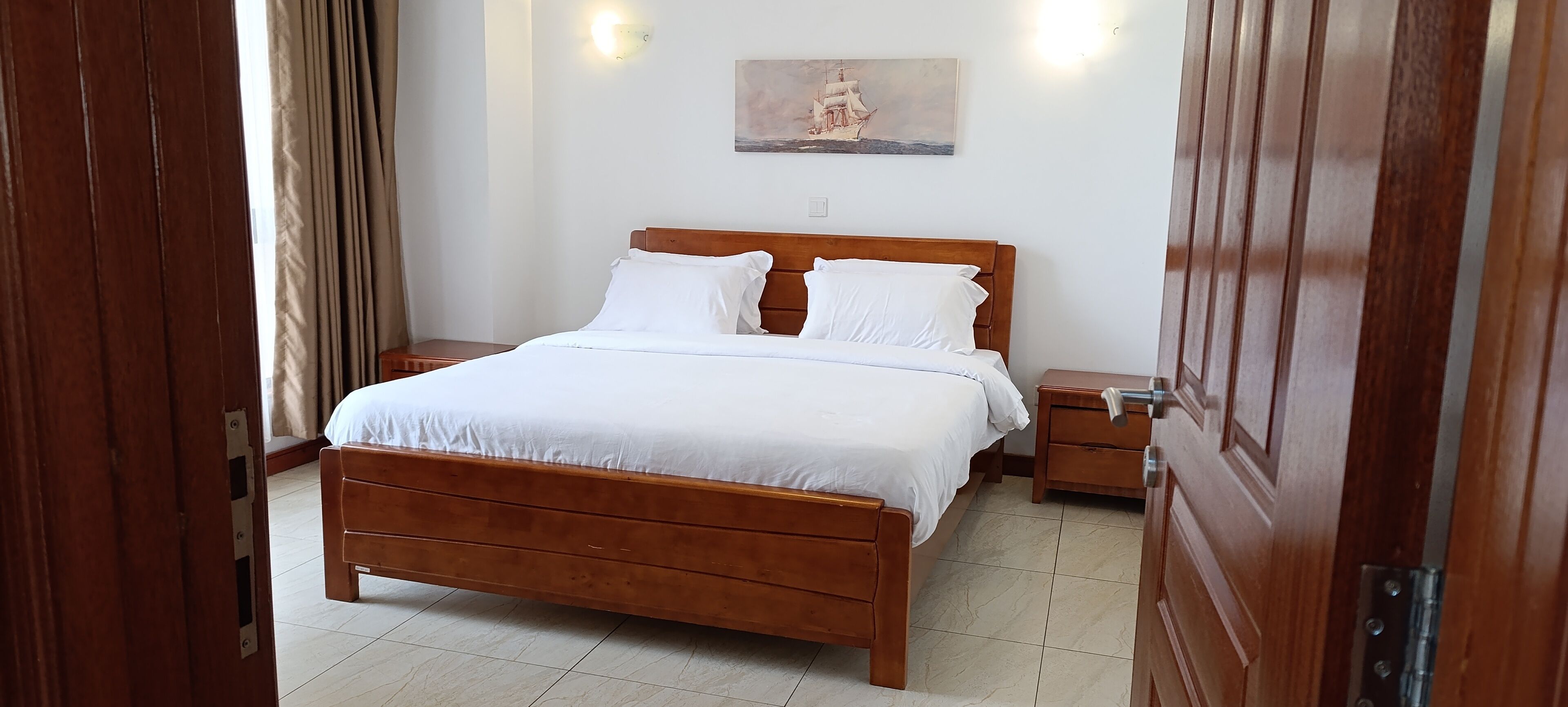 A neatly made bed with white linens, a wooden headboard, and a nightstand with a lamp.