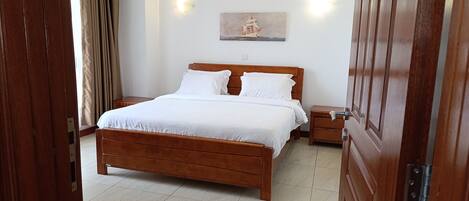 A neatly made bed with white linens, a wooden headboard, and a nightstand with a lamp.