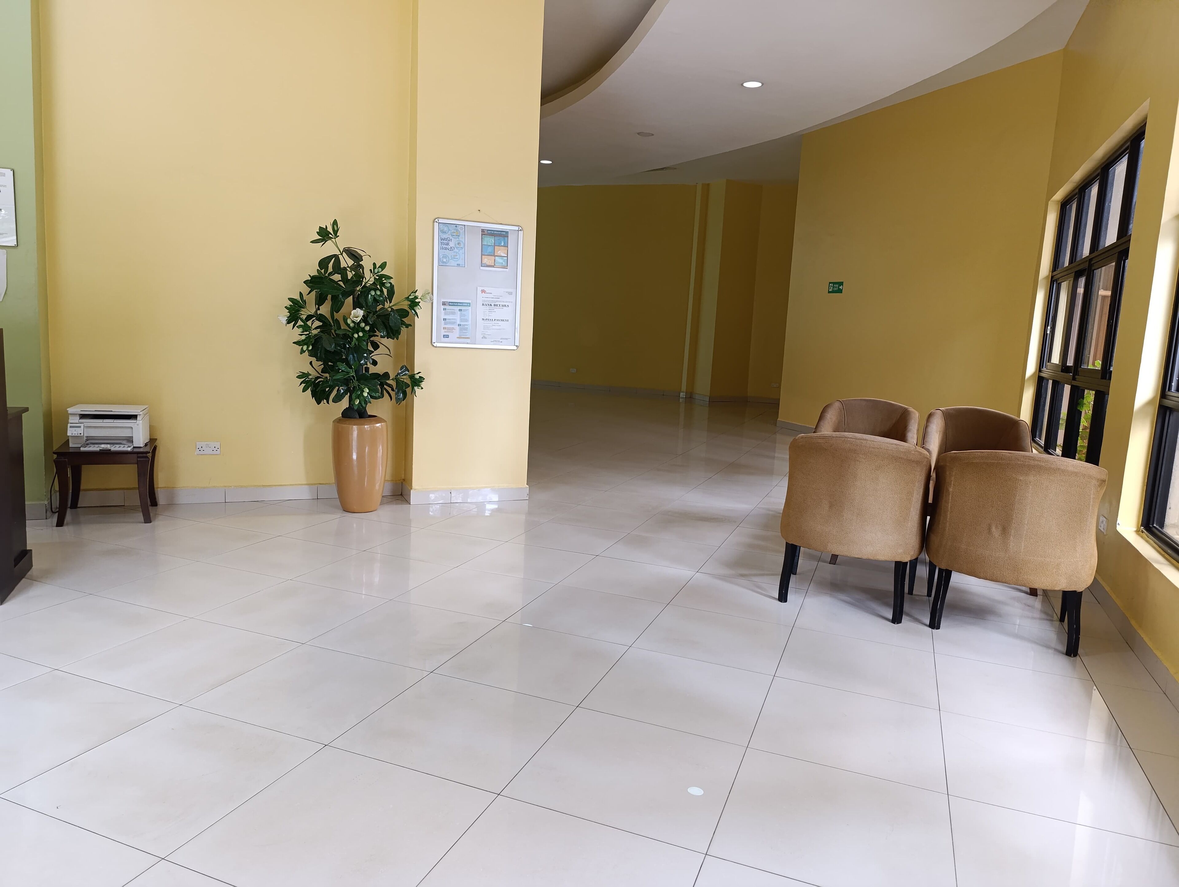 Een ruime lobby met een receptiebalie, een potplant en een zithoek met stoelen.